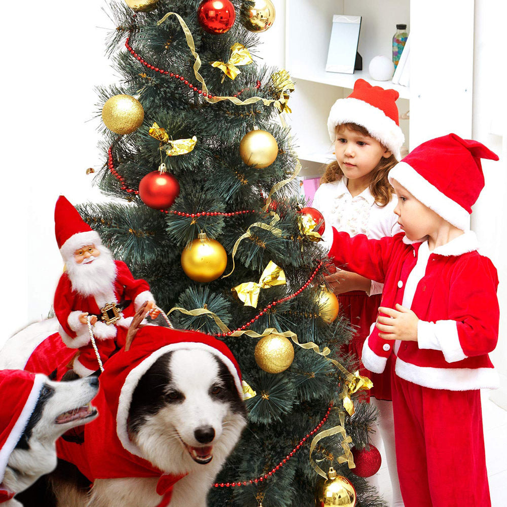 Dog in a red Santa Riding Reindeer costume beside two children in Santa outfits by a decorated Christmas tree